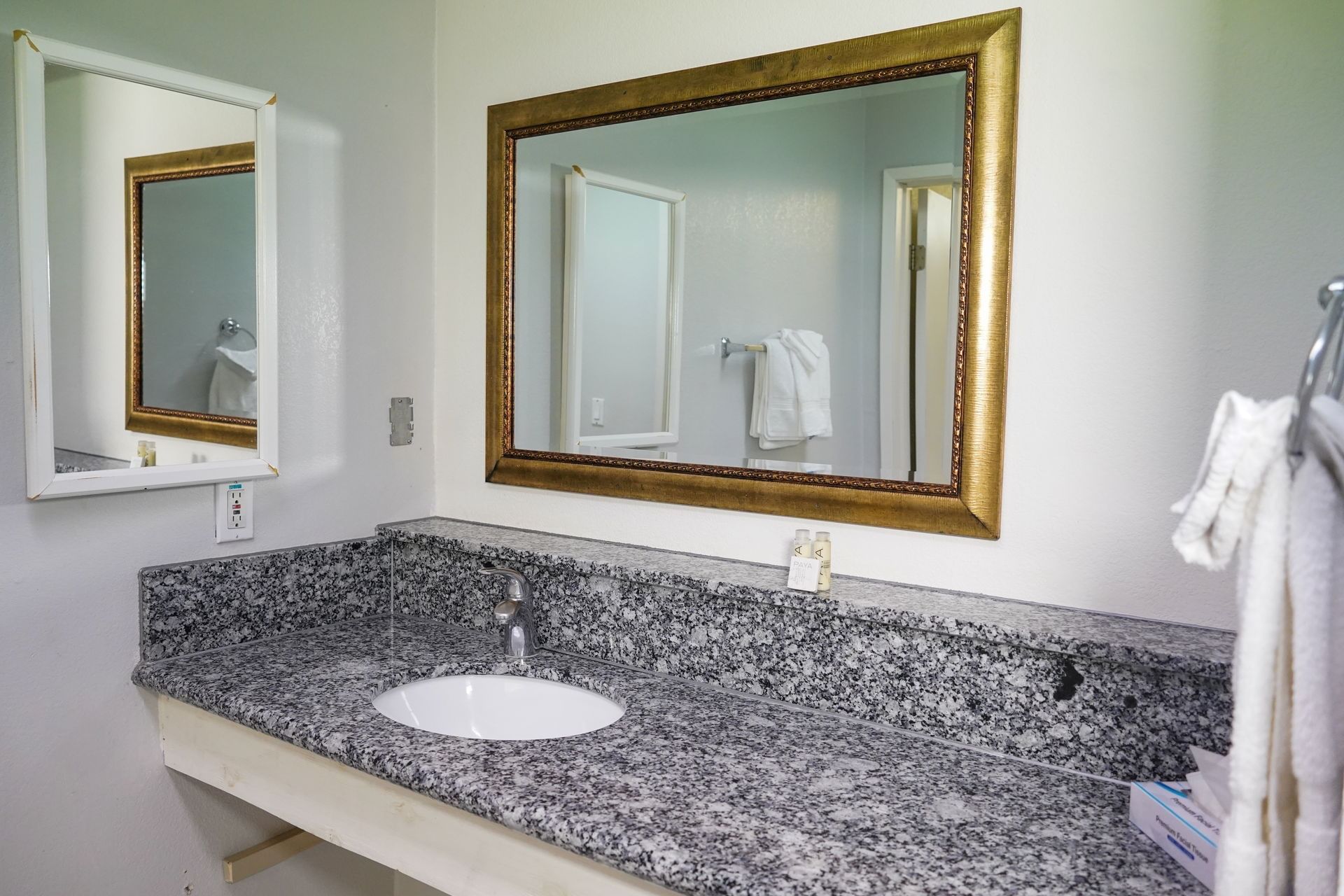 A bathroom vanity with a granite countertop, single sink, and gold-framed mirror.
