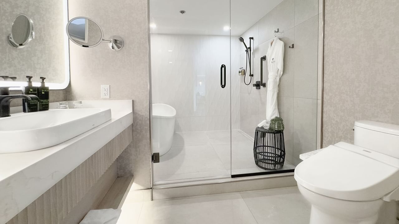 Hotel washroom with toilet, sink, bath tub, shower,  soap, and towels