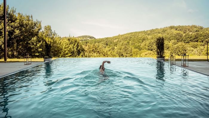 A person swimming in a pool overlooking the hills at Falkensteiner Balance Resort Stegersbach