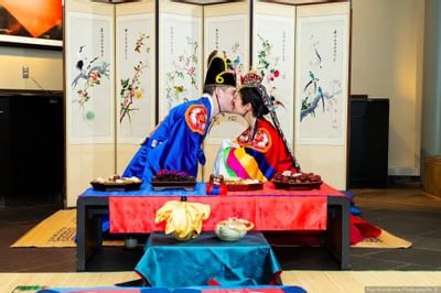 Couple in traditional Korean wedding attire sharing a kiss at a ceremony table at Aramark Chauncey Conference Center
