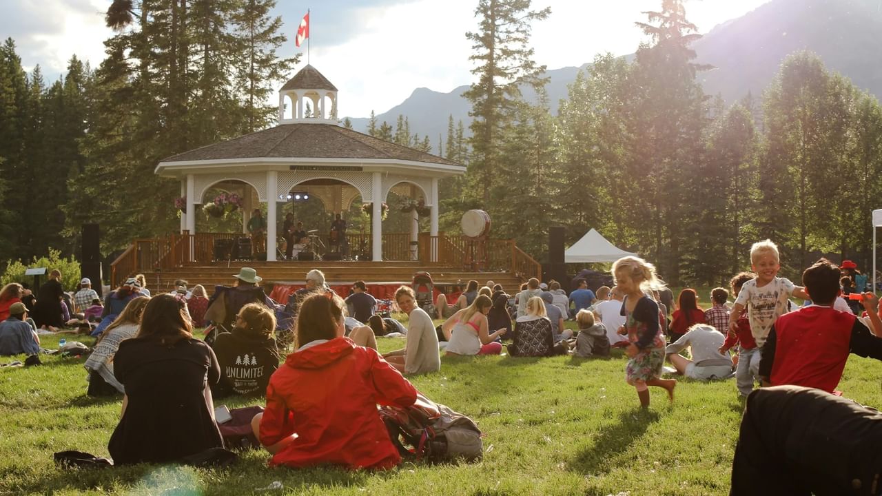 People enjoying outdoor activities with kids and musicians in gazebo on sunny day.