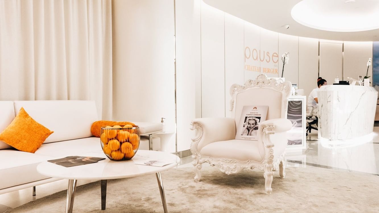 Stylish waiting room with a couch, ornate chair, & orange cushions in Pause Spa Chateau Berger at Paramount Hotel Dubai