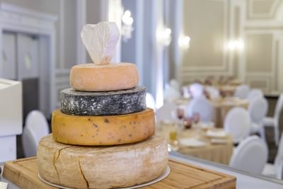 Tiered cheese wheels on a wooden board by dining tables at Rodd Charlottetown Hotel, a featured Charlottetown event venue
