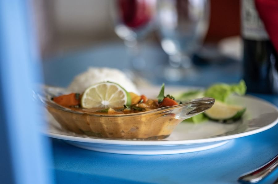 Close-up of a glass bowl of orange curry and rice on a blue table in Tambua Restaurant at Tambua Sands Beach Resort