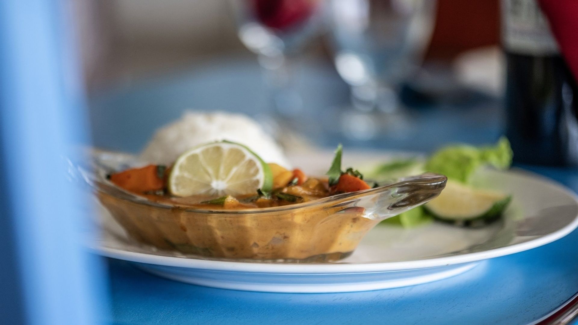 Close-up of a glass bowl of orange curry and rice on a blue table in Tambua Restaurant at Tambua Sands Beach Resort