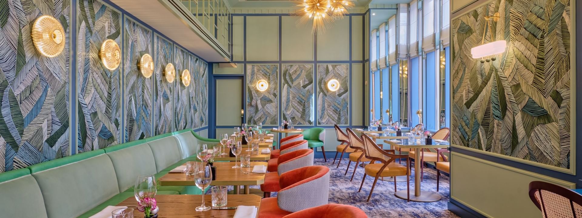 The Restaurant at the Capital interior featuring green banquettes, chairs, leafy wallpaper, and starburst light fixtures