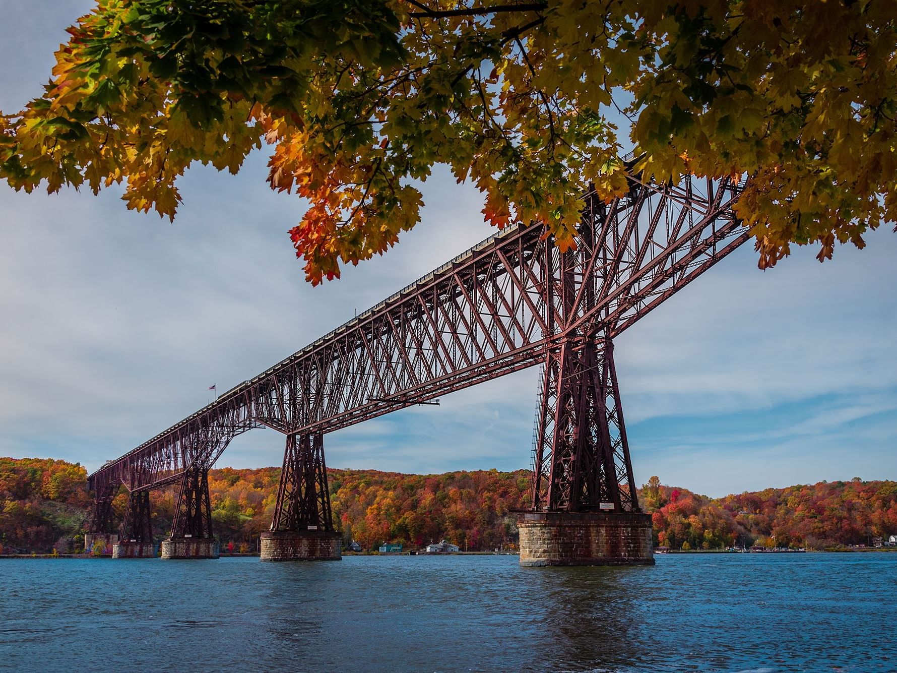 Large railroad bridge spanning a river, with shores lined by colorful autumn foliage near High Peaks Resort
