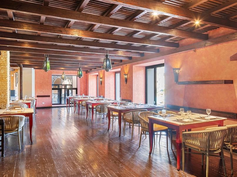 A restaurant with wooden tables, chairs, and ceiling, orange walls, and glass doors with windows.