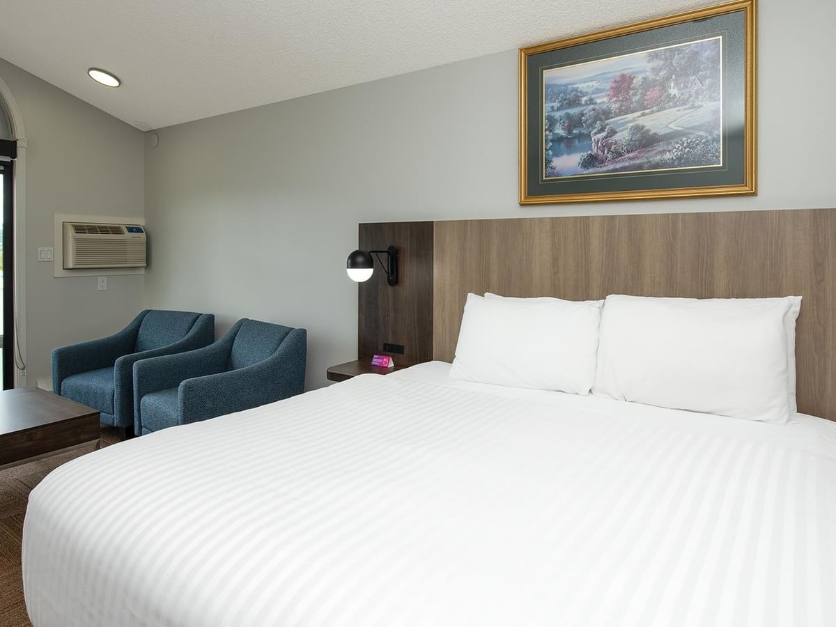 Coast King room with white bedding, wood headboard, blue armchairs and balcony.