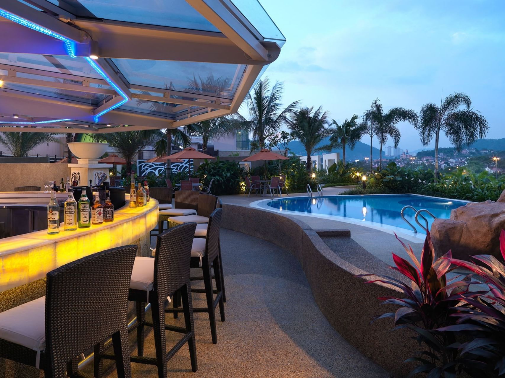 Outdoor bar with black chairs next to the pool area at night in One World Hotel