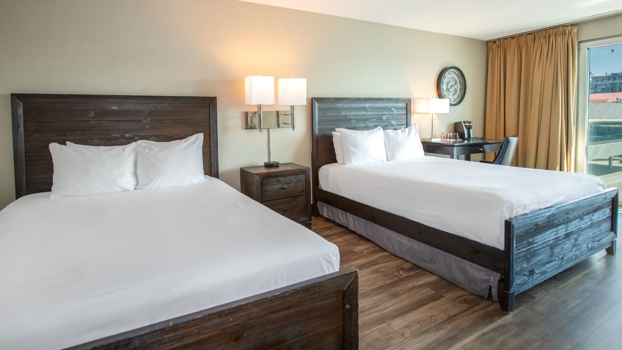 Coast Two Queens room with two queen beds, nightstands with lamps, and a desk near a glass door at Coast Lonsdale Quay Hotel