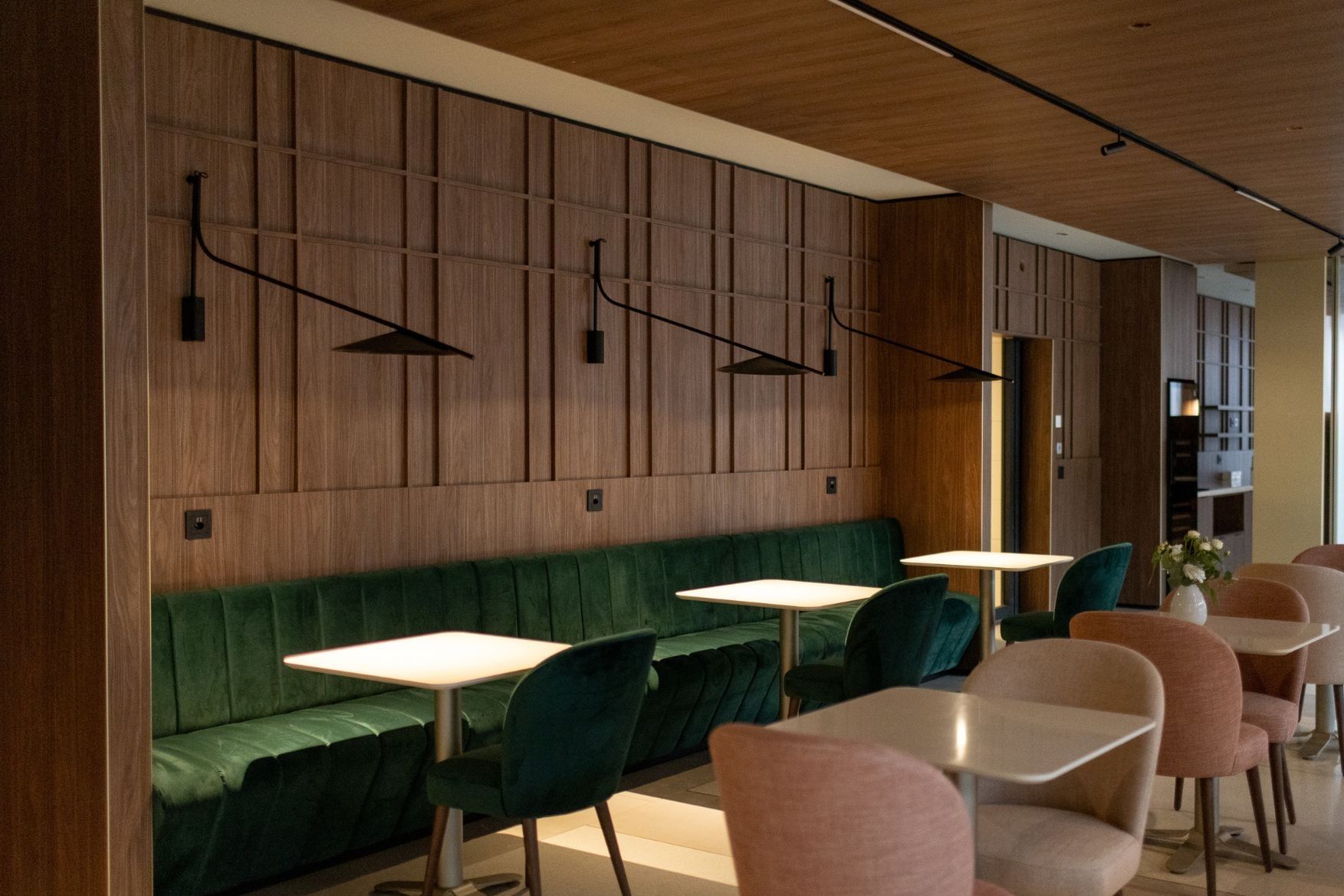 Rich wooden wall paneling and a plush green velvet banquette in a cozy dining area at Hotel des Innovations