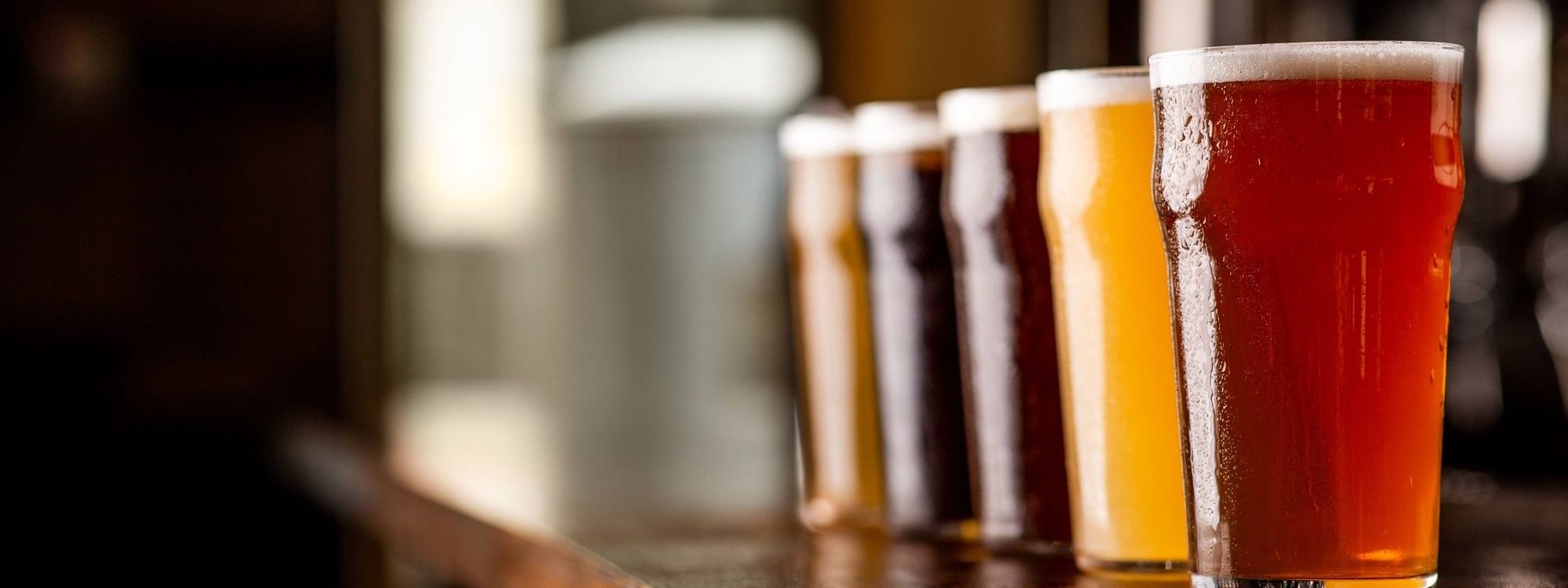 Close-up of a variety of beers served in glasses on a wooden bar counter at Warwick Hotels and Resorts