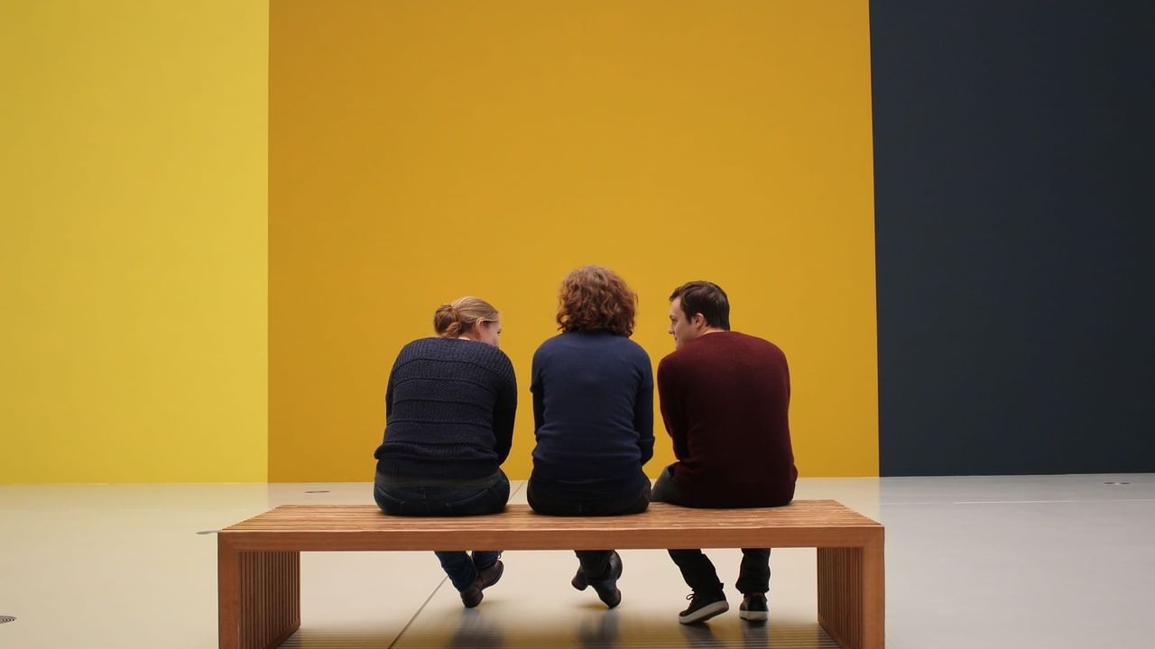 Three people sitten on bench in art museum