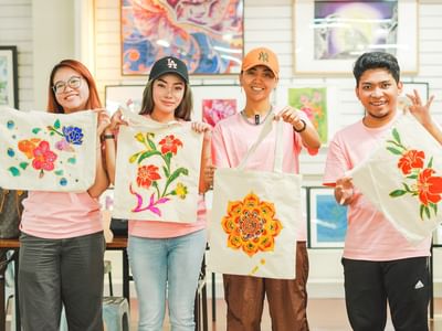 Four people display colorful Jadi Batek tote bags in an art studio.