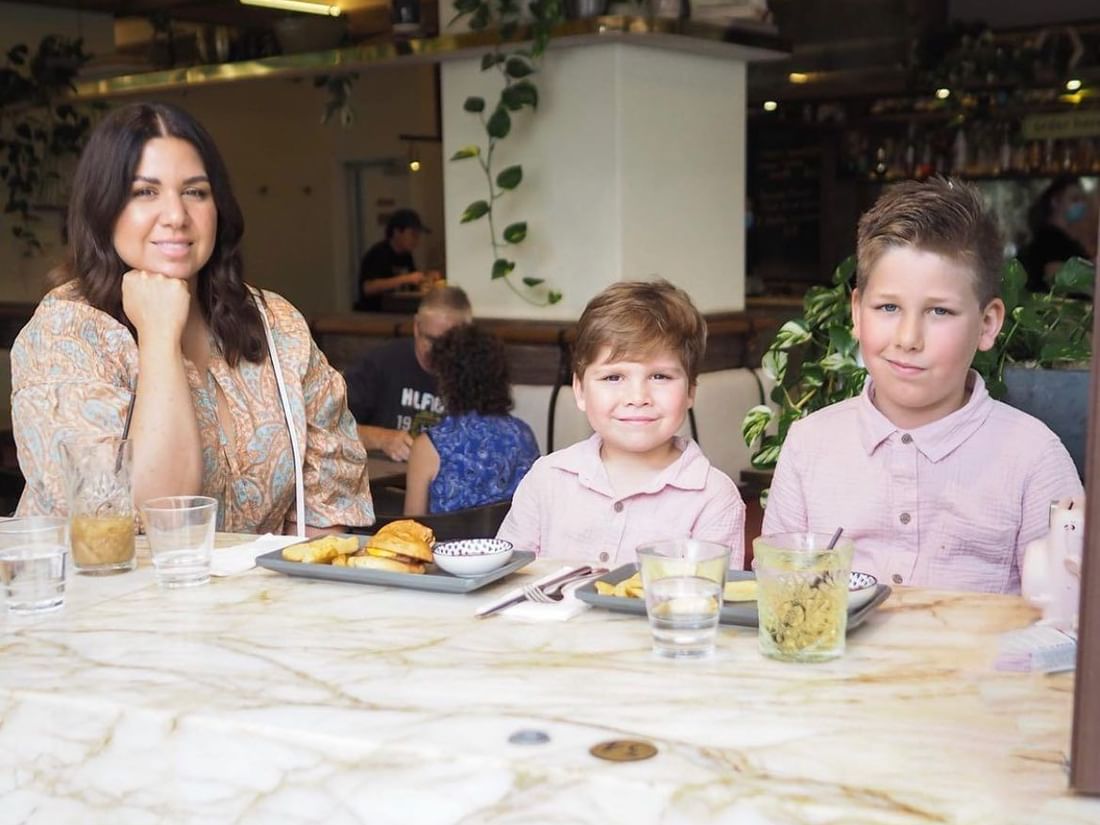 Mother and two boys enjoying a relaxing family meal at a marble-top table inside a casual restaurant at The Sebel Brisbane