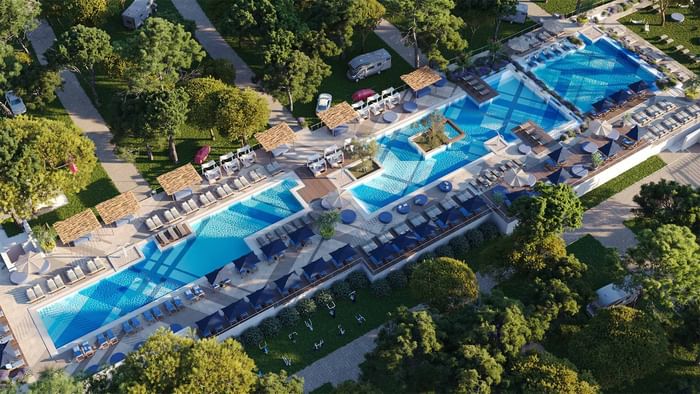 Aerial view of a resort with multiple pools, lounge chairs, and surrounding greenery.