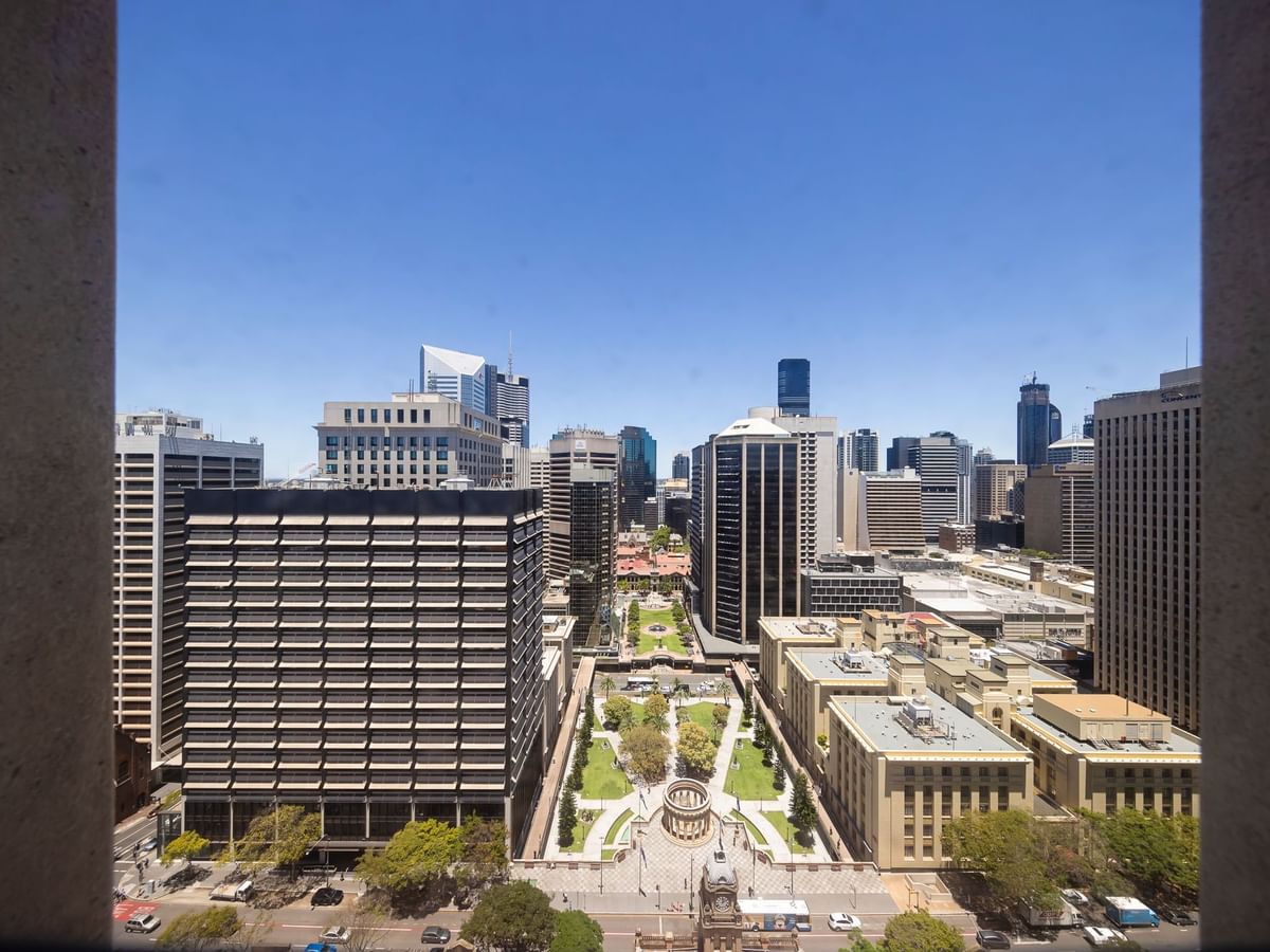 Cityscape framed by stone columns with buildings and a green square under a blue sky at Sofitel Brisbane Central