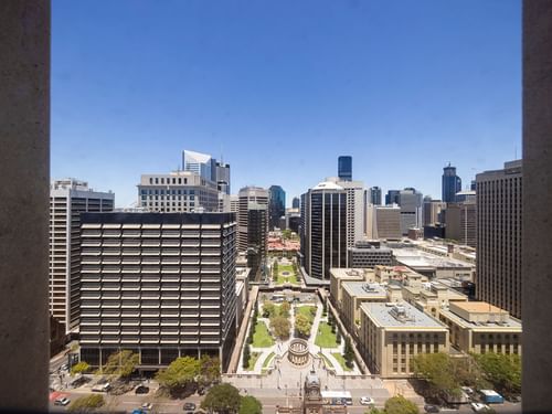 Cityscape framed by stone columns with buildings and a green square under a blue sky at Sofitel Brisbane Central