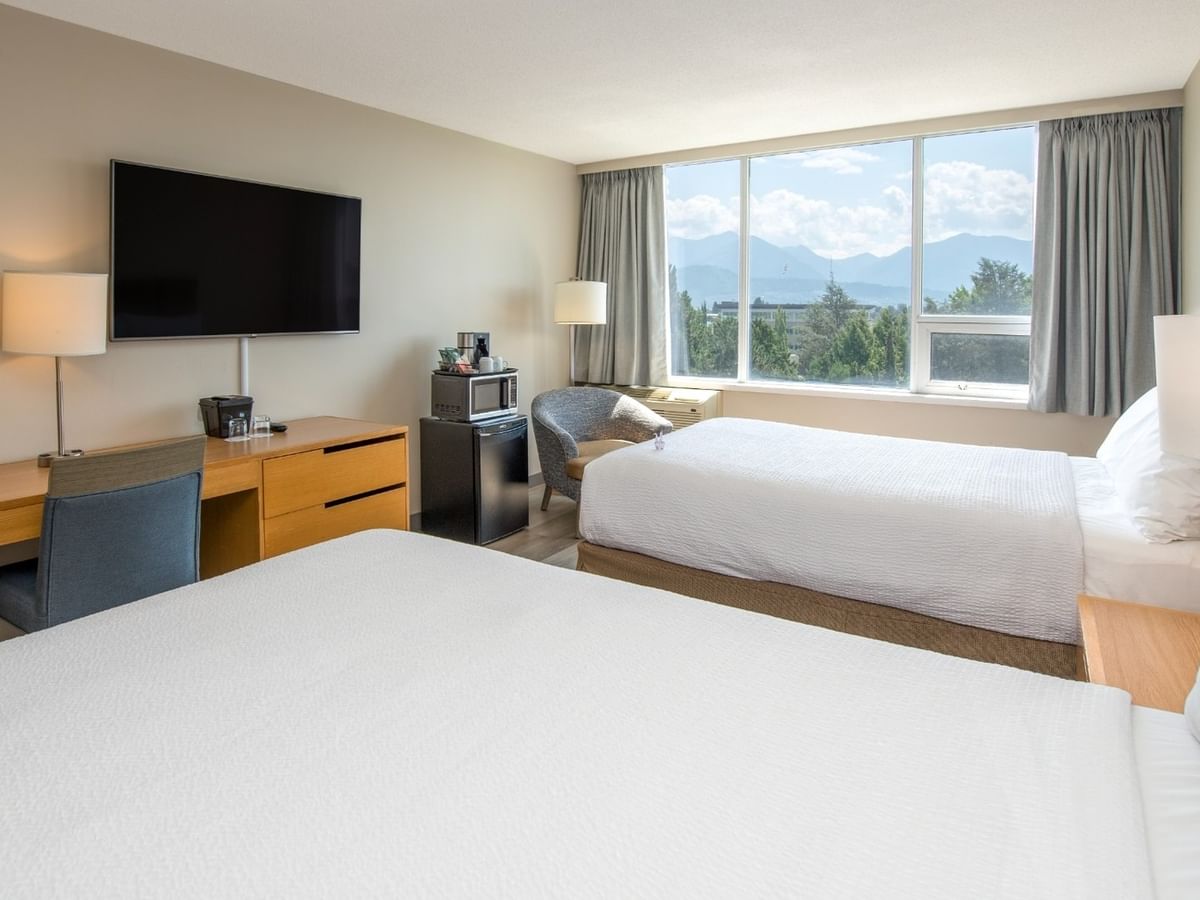 A hotel room with two beds, work desk with lamp, chair, TV, and large window with pond view.