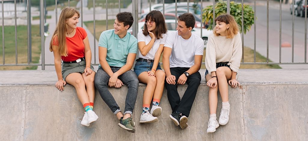 five teenagers sitting on a curb