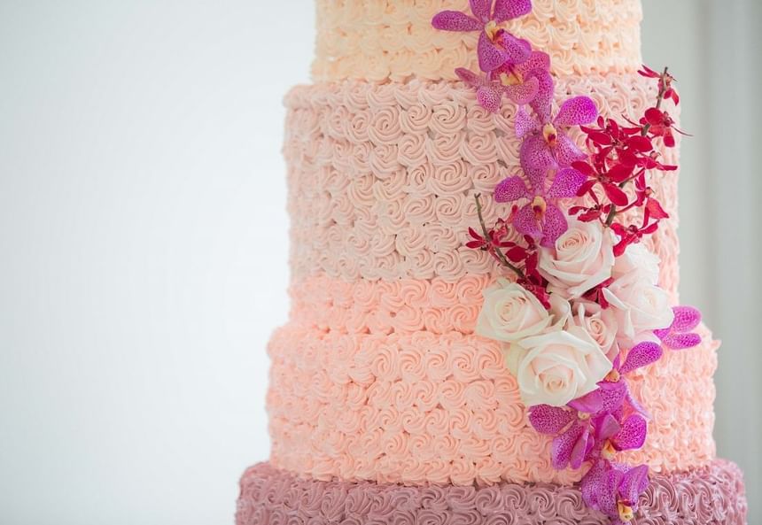 Three-tier cake with pink and peach rosette icing, adorned with white roses and vibrant orchids at Park Hyatt Saigon