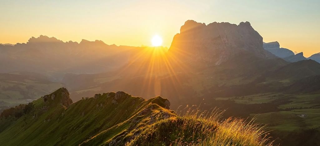 Golden sunrise casting light over lush green mountain ridges and valleys in the Canadian Rockies