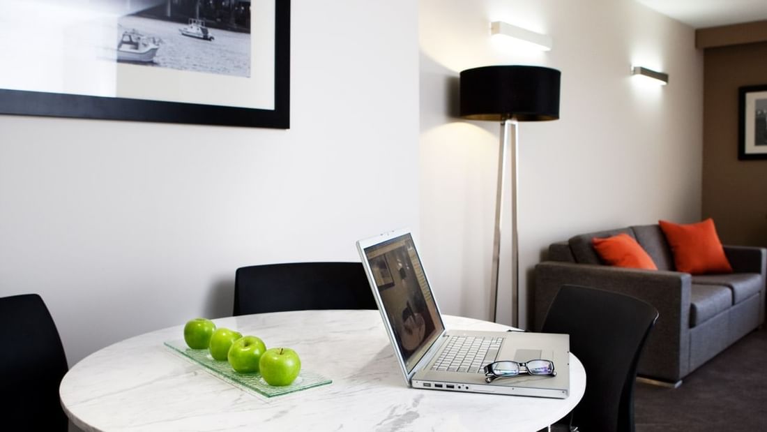 Work area with a round table, laptop, and sofa in Deluxe Suite at Novotel Sydney International Airport