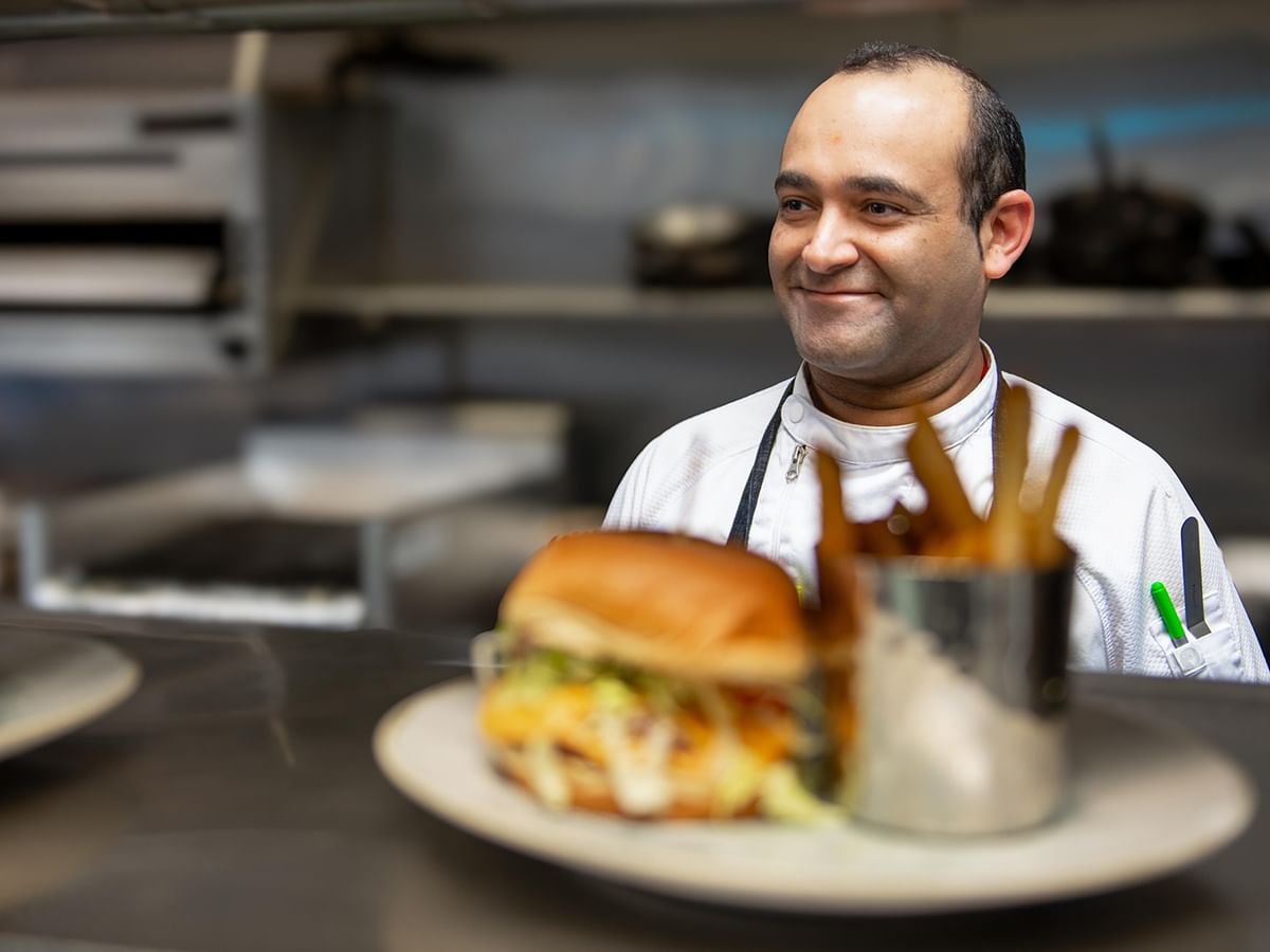 Chef smiling behind plate of burger and fries.