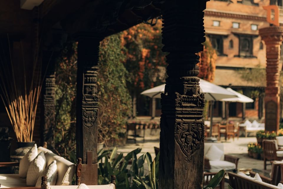 Intricately carved wooden pillars frame a serene outdoor dining area at The Dwarika’s Hotels and Resorts