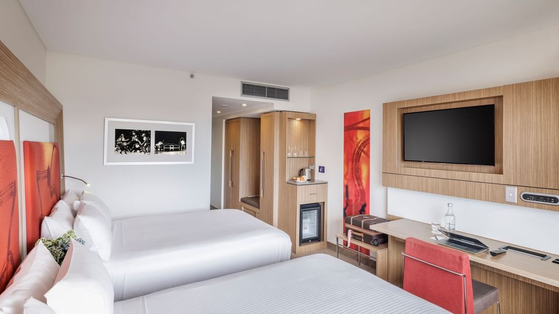 TV, work desk, and cupboard by the beds in Superior Room with vibrant orange artwork at Novotel Sydney Olympic Park