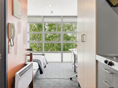 A modern room with a bed, desk, and kitchen area at Student Living Auckland - Beach.