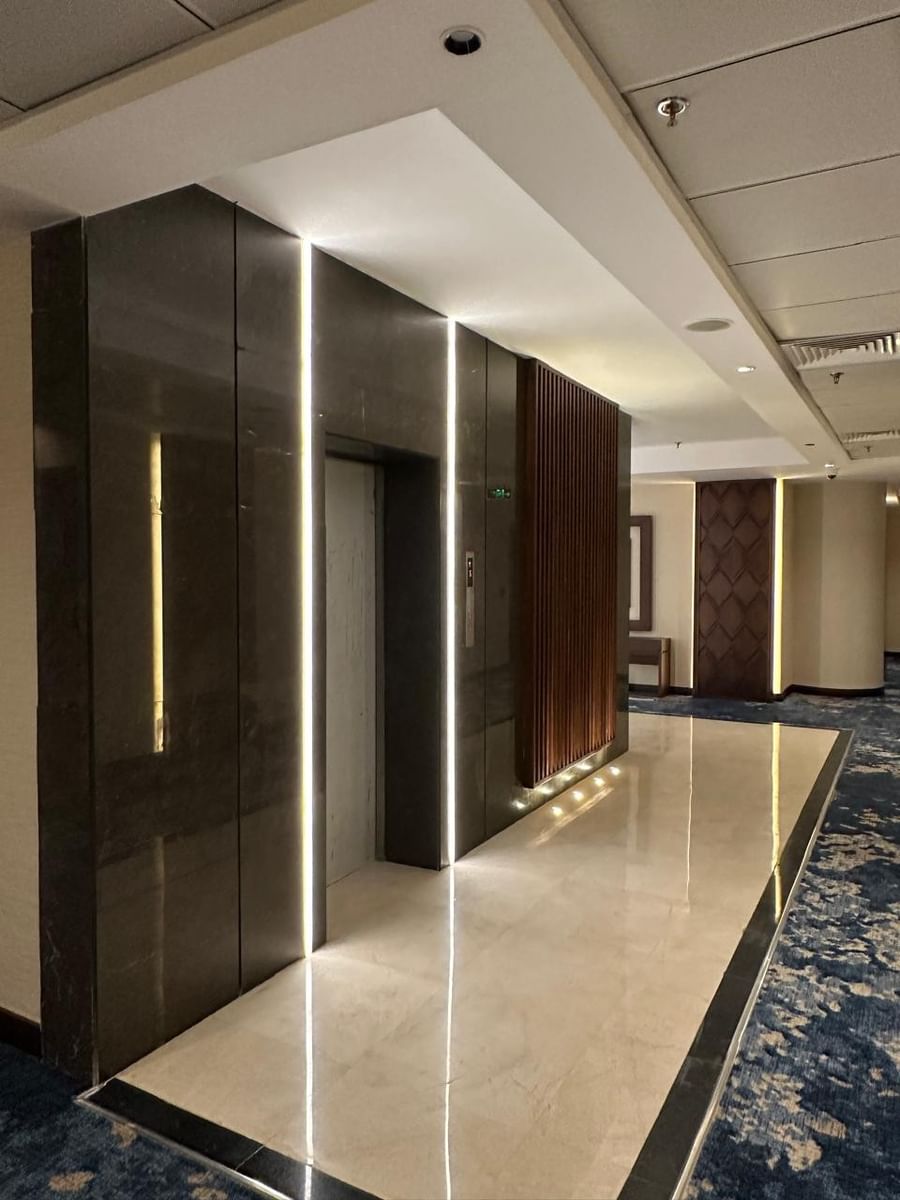 Elevator doors by a dark marble wall under vertical strip lighting in a hallway at Warwick Jeddah Hotel & Spa