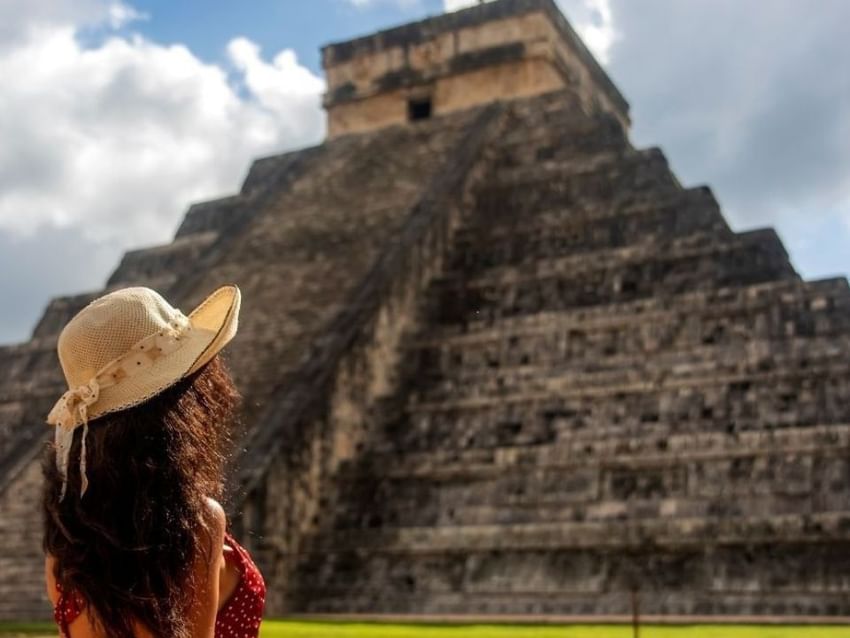 Mujer con sombrero admirando la pirámide de Chichén Itzá cerca de Real Inn bajo cielo nublado