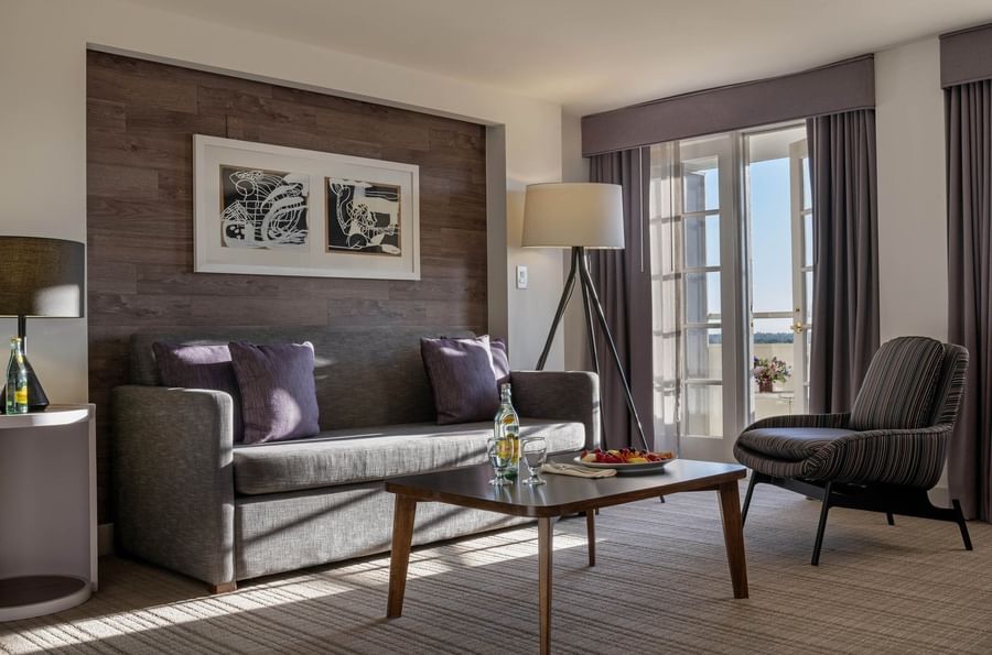 Gray sofa with purple pillows by a tripod lamp under a wood-paneled wall in Executive Suites at Warwick Denver