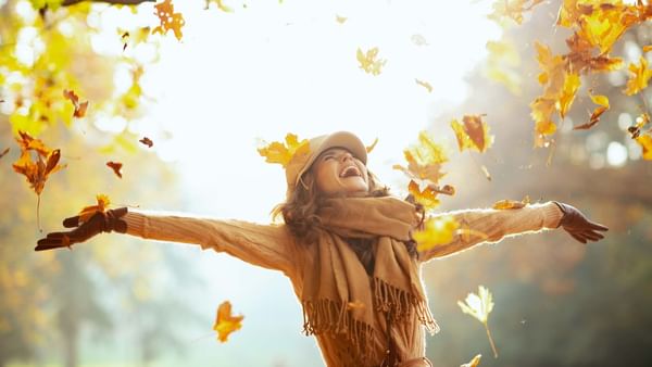 Femme attrapant des feuilles tombantes en automne