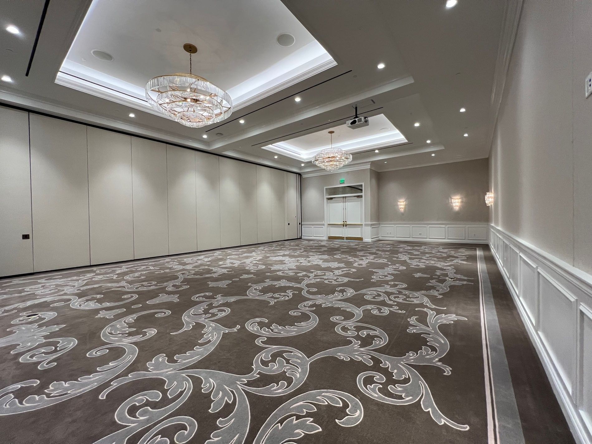 Empty ballroom with a patterned carpet by white paneled walls under chandeliers at Warwick Melrose Dallas