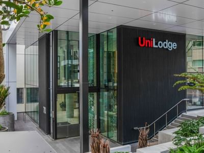 Modern building entrance with glass doors and vertical black cladding displaying UniLodge signage surrounded by greenery
