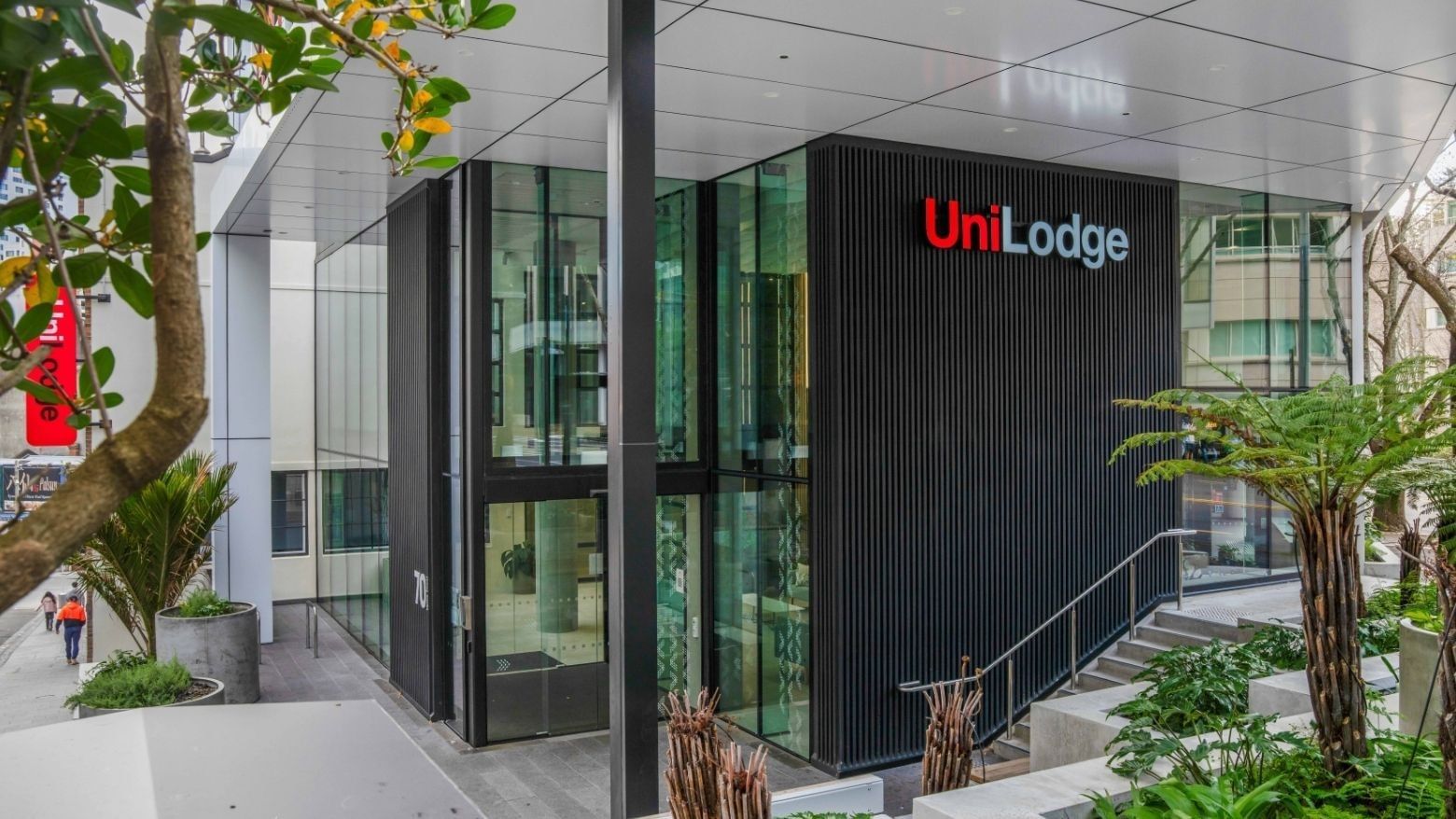 Modern building entrance with glass doors and vertical black cladding displaying UniLodge signage surrounded by greenery