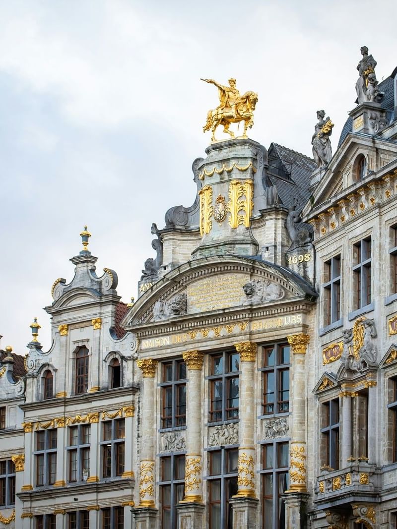 Grand Place facade with golden statues by the roofline and carvings under the eaves near Warwick Grand Place Brussels