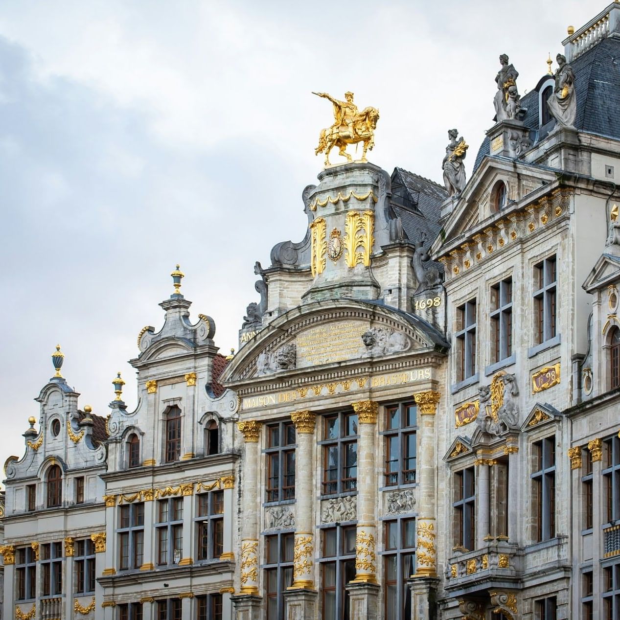 Grand Place facade with golden statues by the roofline and carvings under the eaves near Warwick Grand Place Brussels