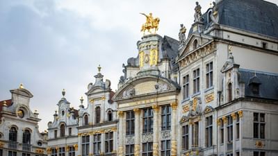 Grand Place facade with golden statues by the roofline and carvings under the eaves near Warwick Grand Place Brussels