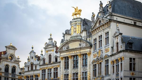 Grand Place facade with golden statues by the roofline and carvings under the eaves near Warwick Grand Place Brussels