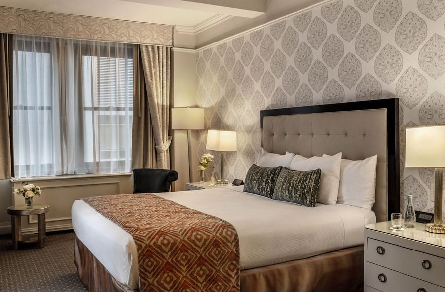 Elegant bedroom with a large bed, floral wall, curtains, and nightstands with lamps at Warwick New York.