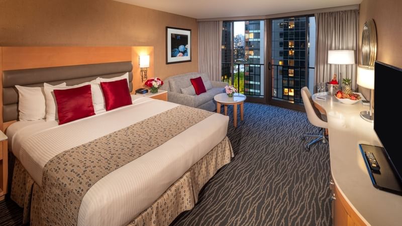 A hotel room with a large bed, a couch, a balcony, and a desk with a TV.