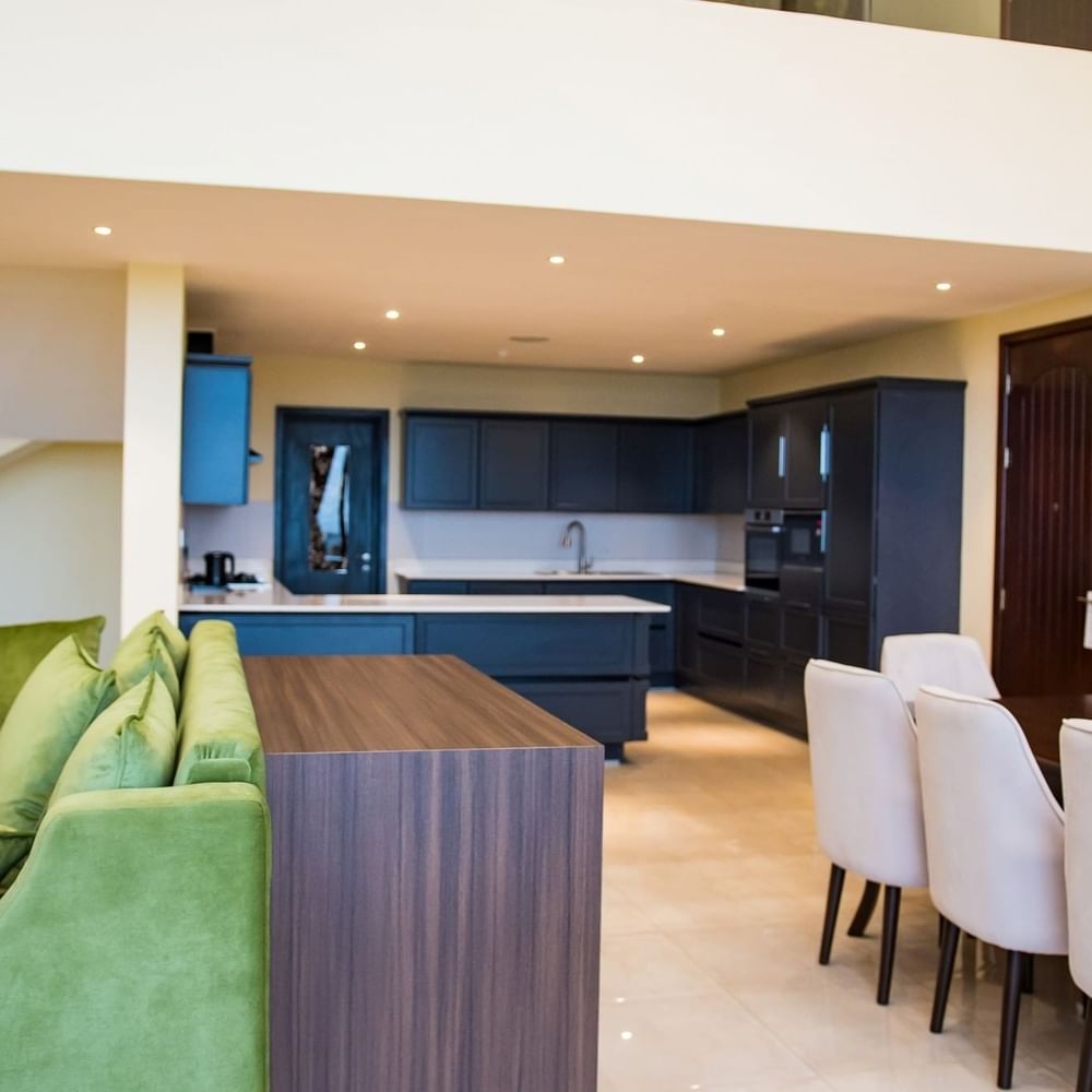 Living room with green couch, wooden table, and modern kitchen at Lake Victoria Serena Golf Resort & Spa, Kampala.