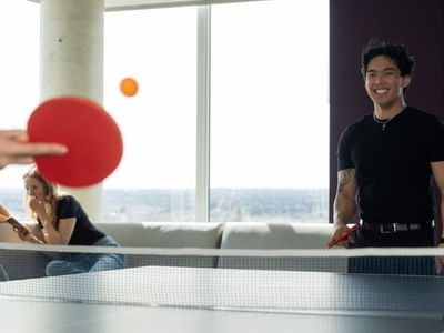 Students playing ping pong and chatting on the lounge chairs, with a view of the sky from floor to ceiling windows.