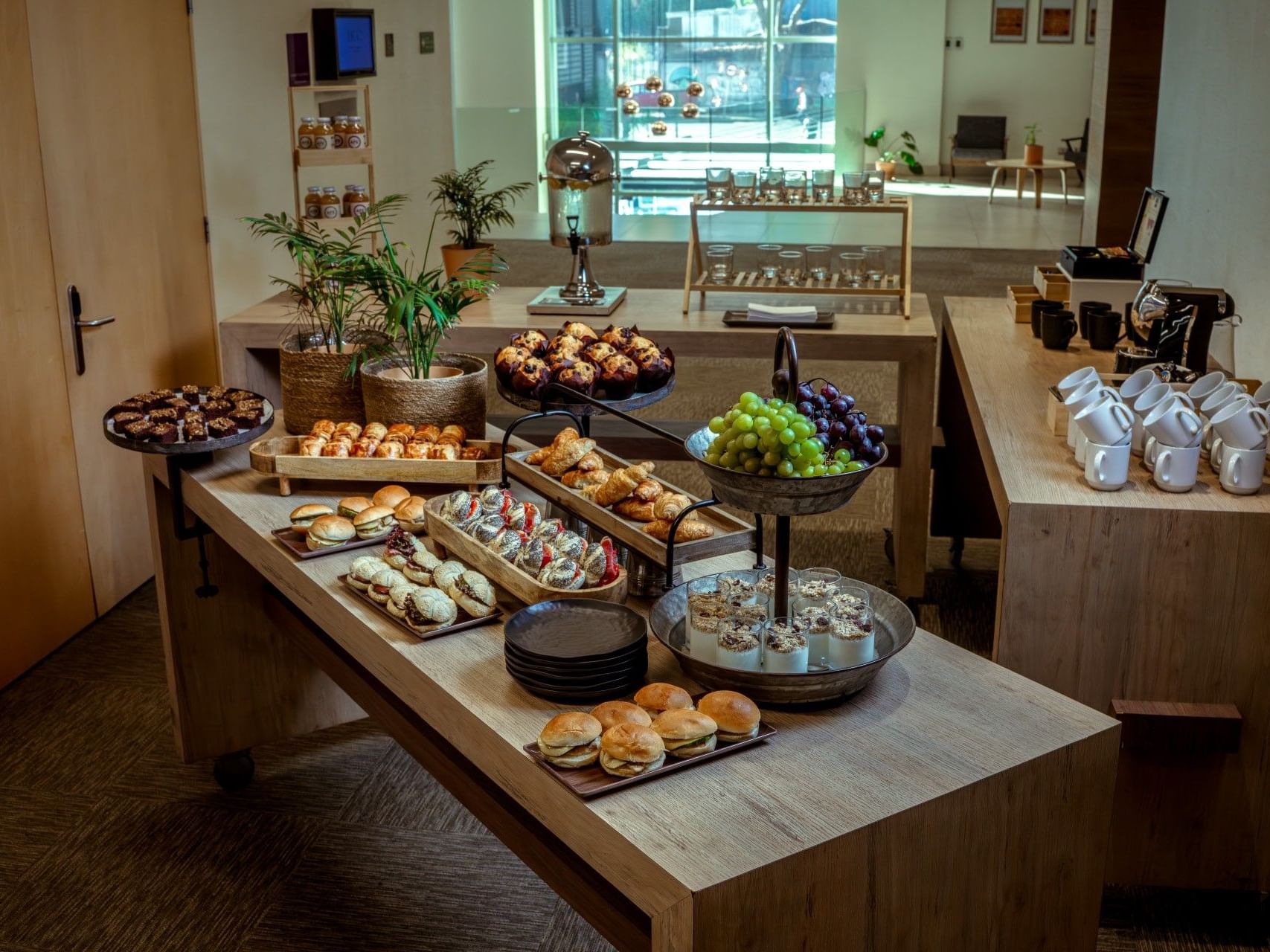 Surtido de pasteles, fruta y bebidas dispuestos sobre una mesa de madera en el hotel HCC Costanera Concepción.