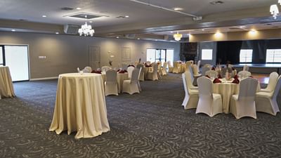 Spacious banquet hall with round tables dressed in ivory linens and white chair covers at London Bridge Resort