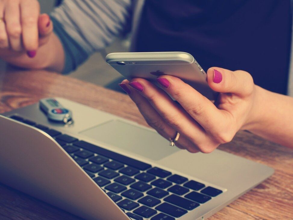 Woman holding phone and on laptop